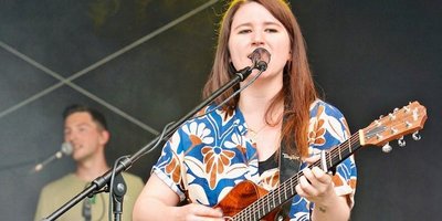 Isabell Krohn Isabell Krohn steht auf der Bühne mit ihrer Gitarre und singt in ein Mikrofon.