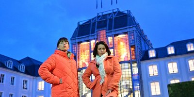 Regionalverbandsdirektorin Dr. Carolin Lehberger und die Frauenbeauftragte des Regionalverbandes, Mirjam Altmeier-Koletzki stehen auf dem Schlossplatz vor dem Saarbrücker Schloss, dessen Festsaal im Mittelbau anlässlich des Internationalen Tages zur Beseitigung von Gewalt an Frauen in orangefarbenem Licht strahlt