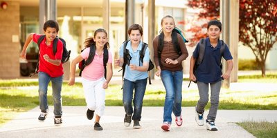 Schulwegweiser Fünf Grundschulkinder verlassen mit ihren Ranzen die Schule und rennen der Kamera entgegen
