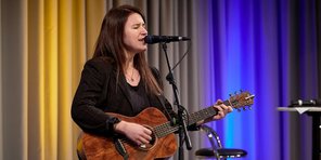Die Preisträgerin Isabell Krohn (EASY) trat zunächst solo mit Gitarre auf. Die Sängerin Isabell Krohn tritt mit Gitarre auf der Bühne des Festsaals auf. Sie hat langes, dunkles glattes Haar und trägt einen schwarz-karierten Blazer.