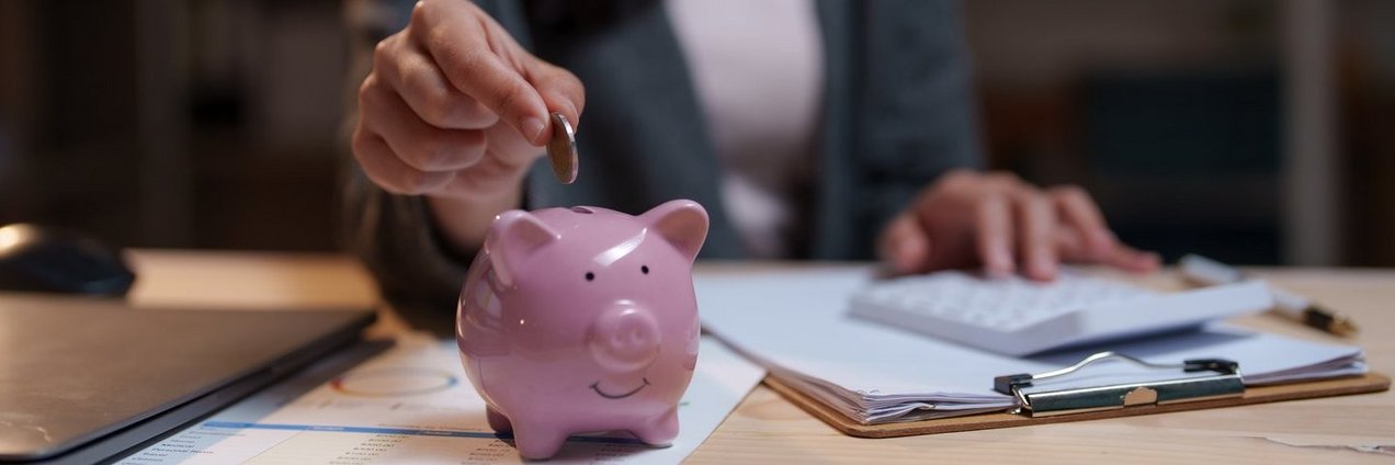 Frau wirft Geld in Sparschwein nachdem sie auf Blatt Finanzen durchgerechnet hat Frau wirft Geld in Sparschwein nachdem sie auf Blatt Finanzen durchgerechnet hat