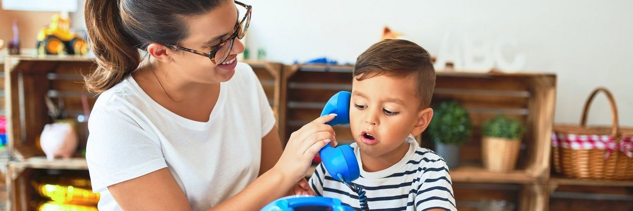 Erzieherin und kleiner Junge spielen mit einem blauen Telefon Erzieherin und kleiner Junge spielen mit einem blauen Telefon