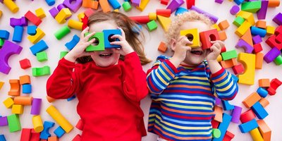 Kleinkinder spielen mit Bauklötzen und halten sich jeweils zwei Bauklötze wie eine Brille vor die Augen