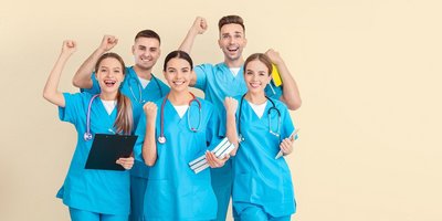 Junge jubelnde Auszubildende im medizinischen Bereich mit Büchern und Klemmbrett in der Hand sowie in blauer Krankenhauskleidung vor einem hellen Hintergrund