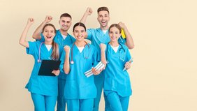 Junge jubelnde Auszubildende im medizinischen Bereich mit Büchern und Klemmbrett in der Hand sowie in blauer Krankenhauskleidung vor einem hellen Hintergrund