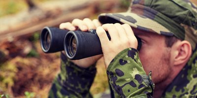 Ein Soldat schaut im Wald durch ein Fernglas