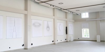 Blick in die leere Remise. An den hellen Wänden hängen große weiße Leinwände mit grauen, minimalistischen Zeichnungen.  