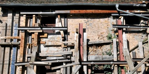 Ein altes, steinernes beigefarbenes Gebäude ist mit zahlreichen Bretten zugenagelt.