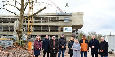 Der Bauherr Regionalverbandsdirektor Peter Gillo (3.v.r.) und Schulleiter Norbert Moy (3.v.l.) freuten sich beim Richtfest gemeinsam mit Bildungsstaatssekretärin Jessica Heide (4.v.r.), dem Völklinger Oberbürgermeister Stephan Tautz (r.), dem Geschäftsführer von arus GmbH, Willi Latz (2.v.r.) und weiteren Vertreterinnen und Vertretern des Regionalverbands und des Ministeriums für Bildung und Kultur. Alle stehen vor dem Rohbau.