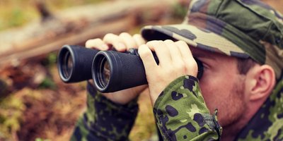 Ein Soldat schaut im Wald durch ein Fernglas